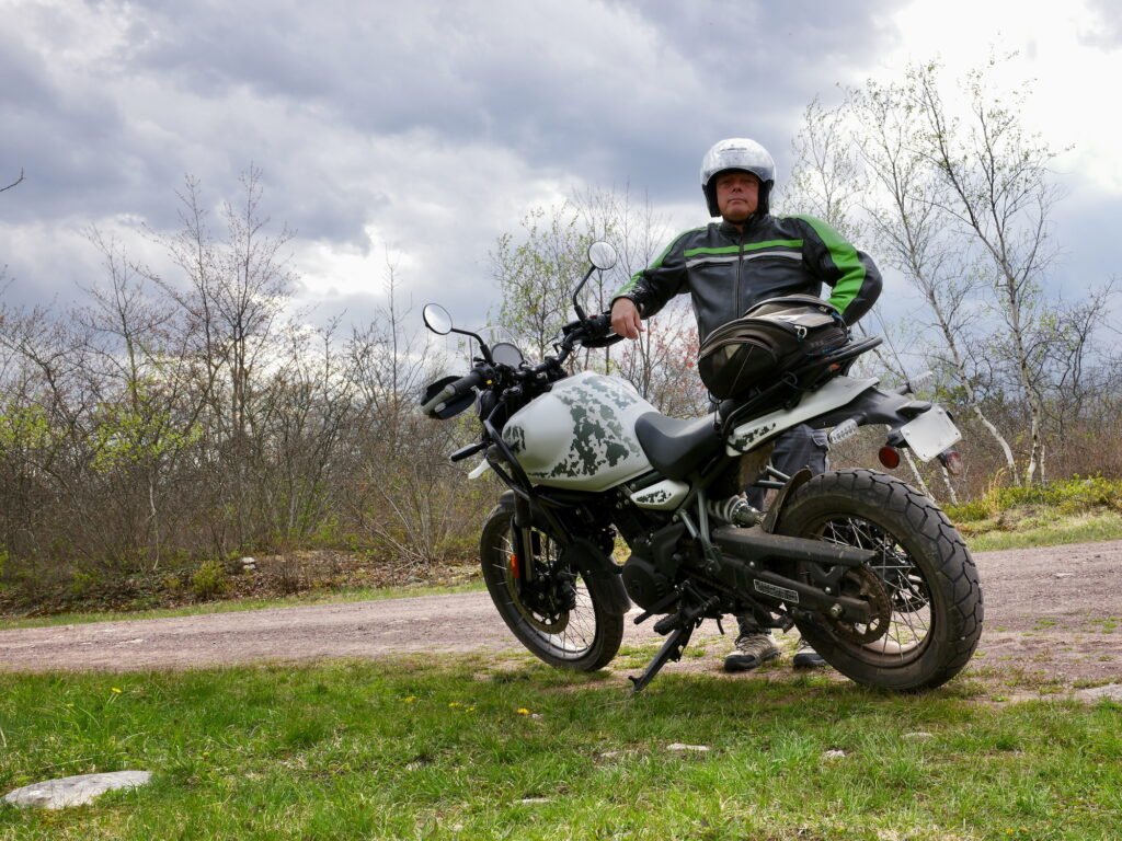 The Mindful Lens Gallery photographer with an adventure motorcycle in a lush green forest landscape.