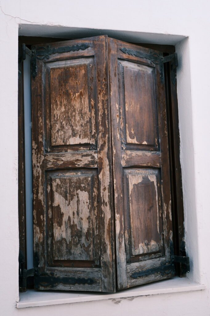 Close-up of old and rustic weathered brown wooden window shutters with rough texture and peeling paint.