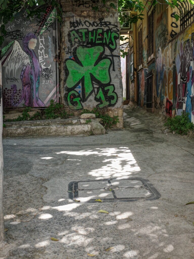 An alleyway corner in Anafiotika with old weathered stone walls covered with multi-colored and fading graffiti.