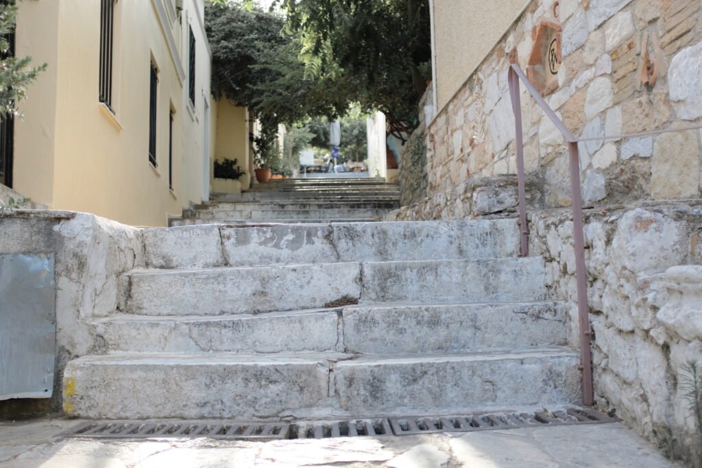Old, weathered and uneven stone steps lead up past stone walls and rustic surroundings toward the village of Anafiotika.