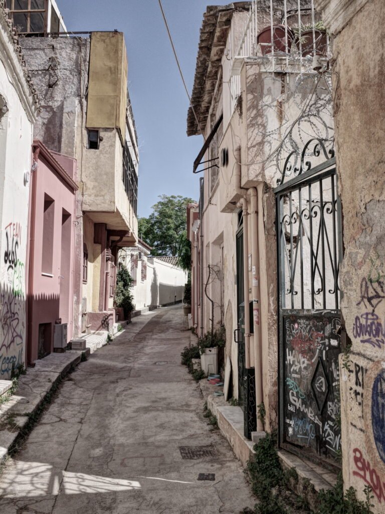 A narrow curving street with signs of dilapidation and graffiti on the rustic walls in Anafiotika.  