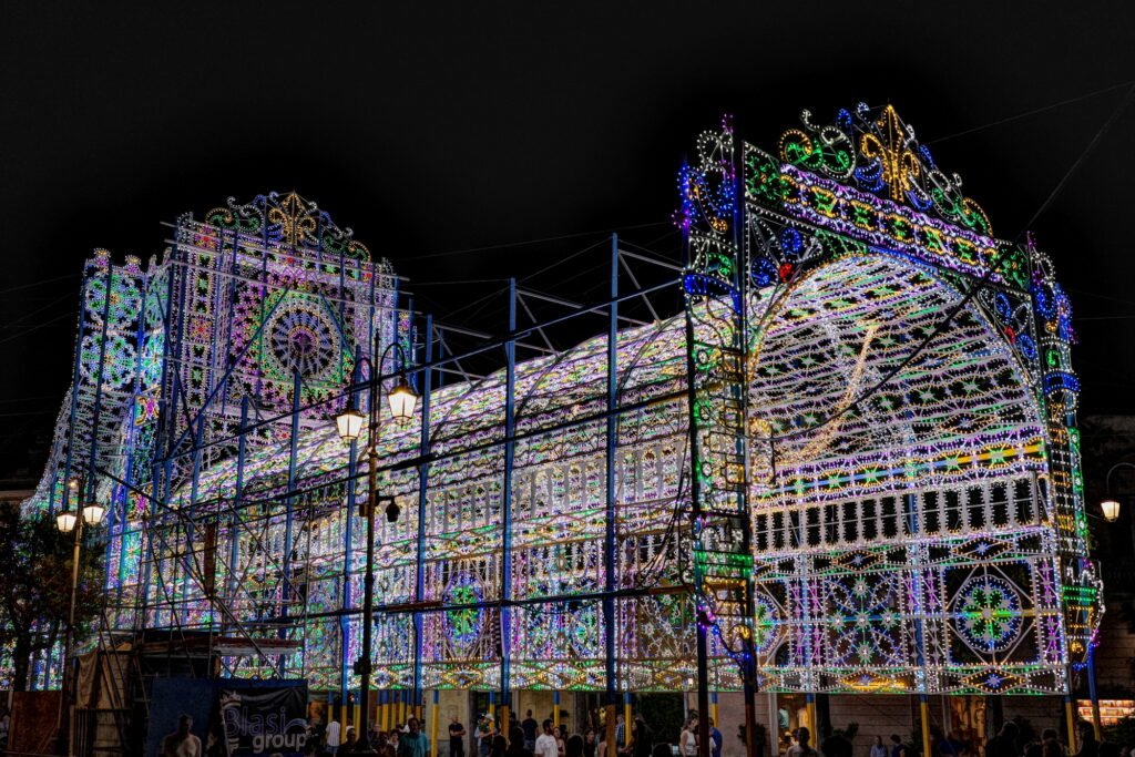 Brigtly colored framework of festive and multicolored lights green, blue, orange and purple over a walkway in Matera, Italy. The metal structure and lights are made with ornate designs.