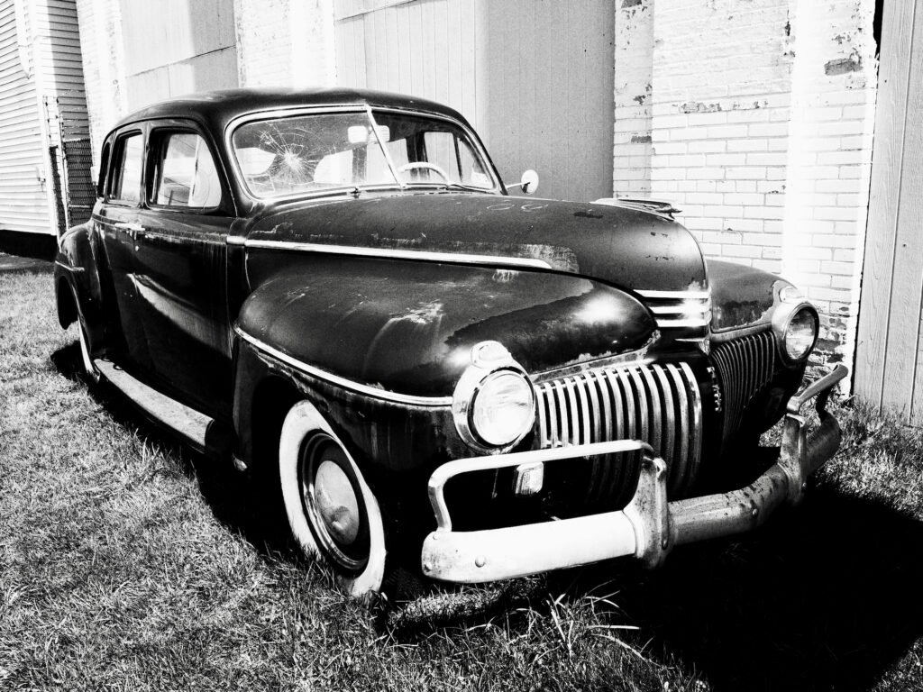 A black and white image of an old 1930's era American car with chrome bumpers and grill and white wall tires.