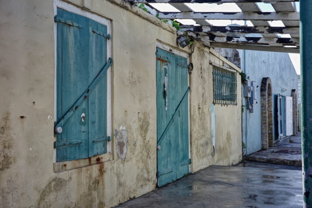 Urban decay in Frederiksted on the island of Saint Croix, USVI, with weathered walls and faded blue wood shutters and blue wooden door with peeling paint.
