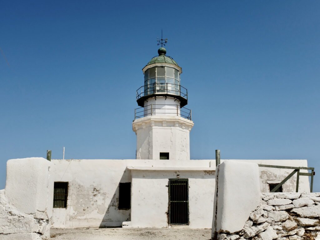 The Armenistis Lighthouse with old whitewashed and weathered walls on the island of Mykonos, with blue sky in the background.