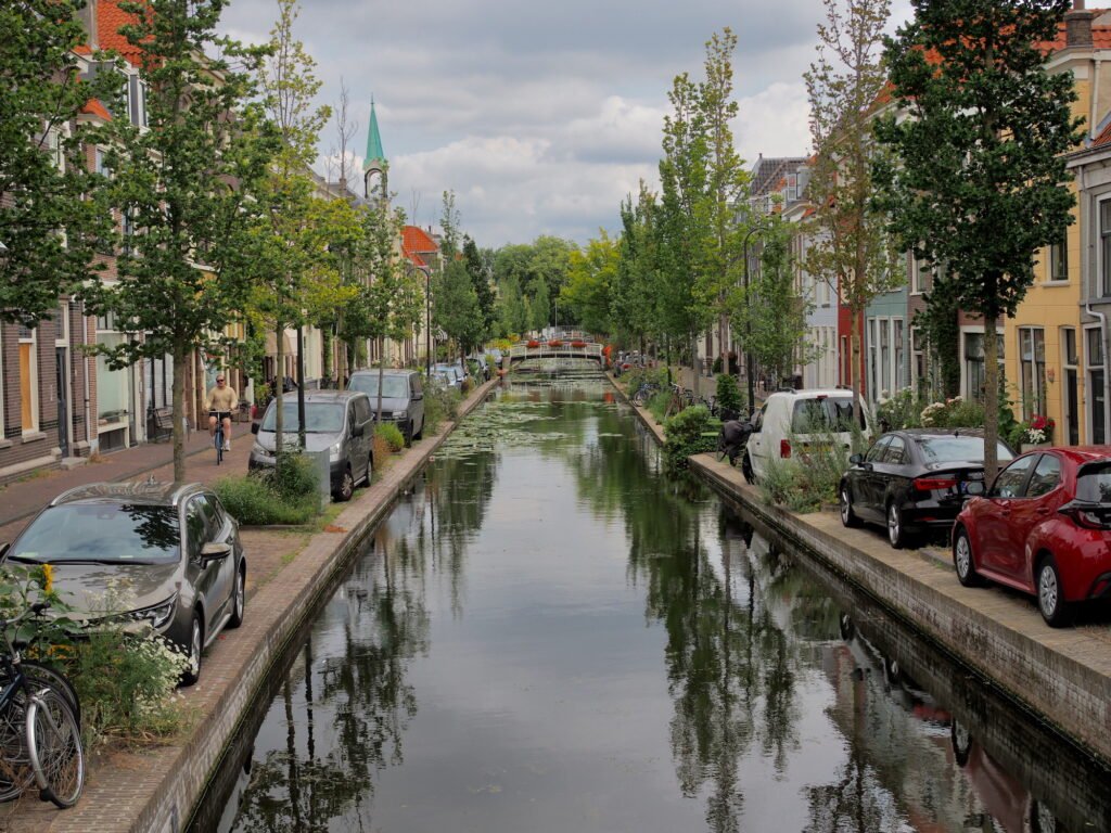 View looking down a residential canal flanked by tree-lined streets and apartment buildings in Delft, Netherlands.
