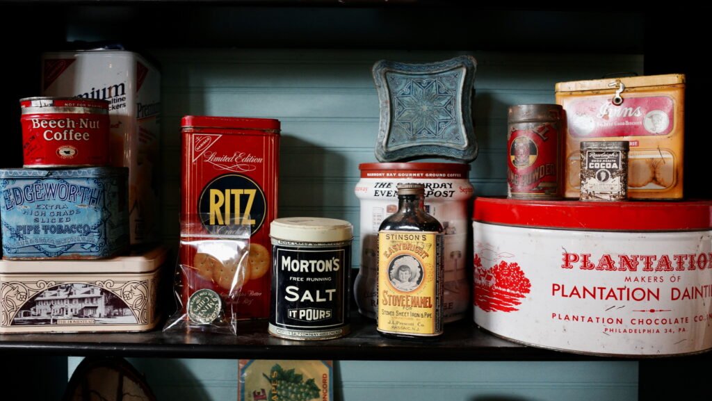 A wabi-sabi style image of old vintage kitchen tins containing coffee, crackers, cocoa and salt, with a dark vignette.