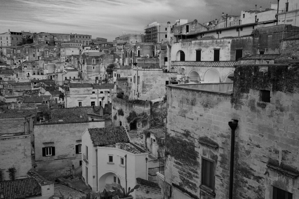 Black and white wabi-sabi travel photography image of the weathered stone homes in the Sassi di Matera. The dwellings pile atop one another in a dense package of wabi-sabi expression in the stone city of Matera.