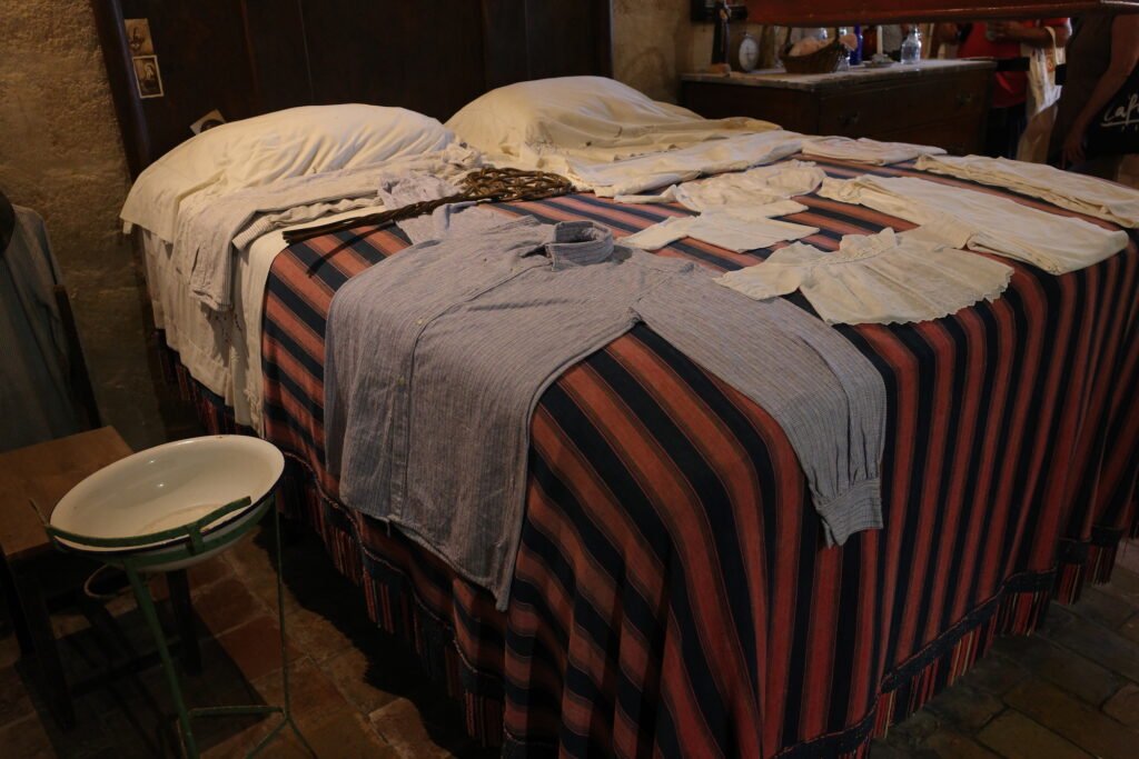 An old rustic bed with period clothes laid out on it and the stone wall in the background in this interior shot of a cave dwelling in the Sassi di Matera.