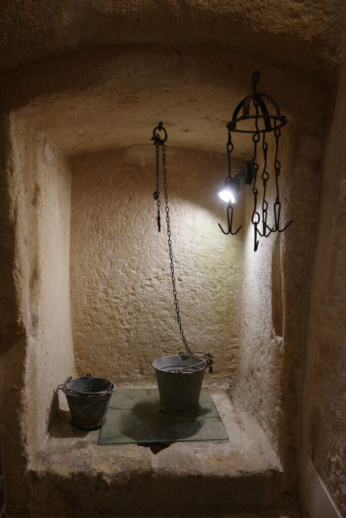 An alcove in a stone wall with buckets and a light in a cave dwelling in the Stone City of Matera.