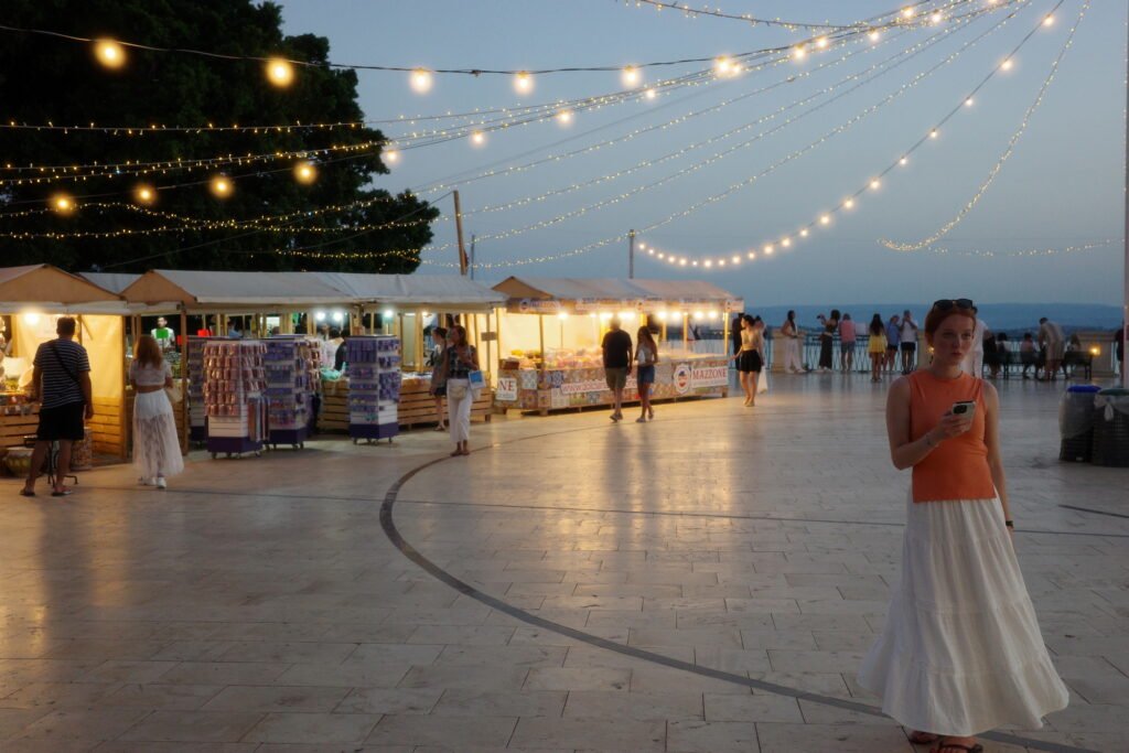 An outdoor market with festive lights and shoppers on the Mediterranean coast of Italy, with festive strings of light hanging over the open square.