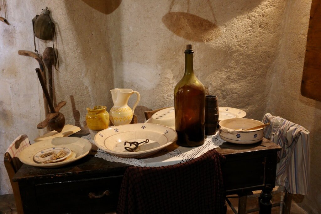 A display of rustic plates, bowls, and bottles with a stone wall in the background in a cave dwelling in the Stone City of Matera.