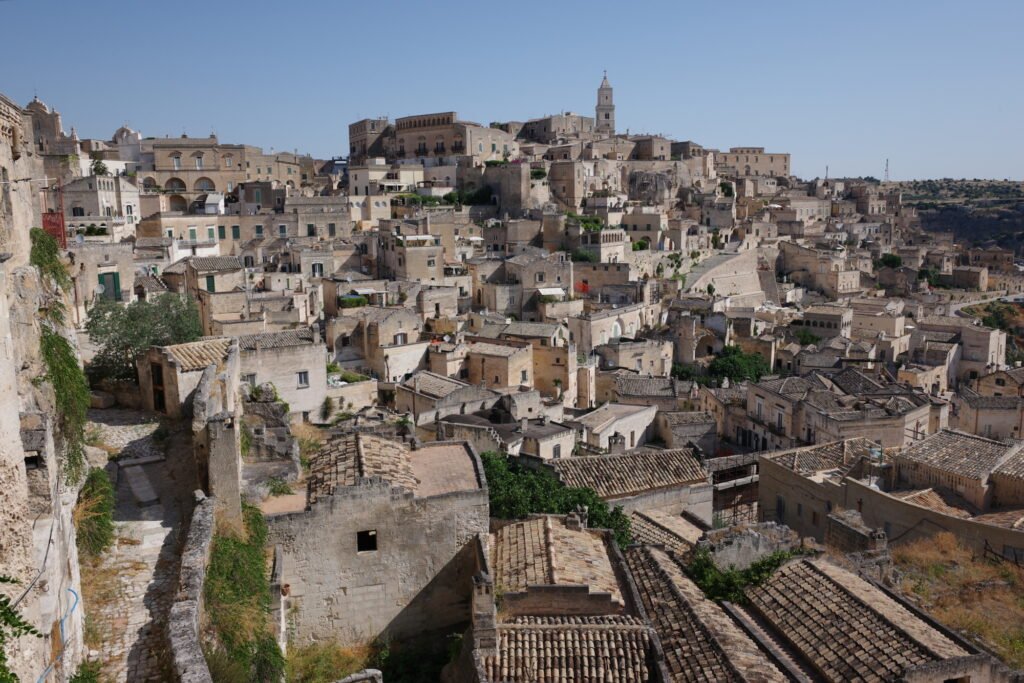 The Stone City of Matera with a view into the Sassi di Matera with its asymmetrical layout of densely packed old homes built into the rock face of the mountain. The view is of an oddly comforting, chaotic harmony and city of wabi-sabi expression.