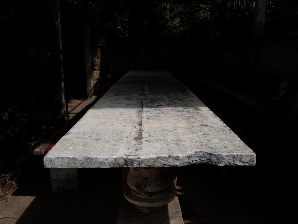Soft sunlight shining on a long weathered stone table top with rough and uneven edges that stretches back into mysterious dark shadows.